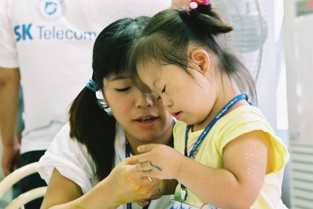 Min Rae Cho, senior vice president of SK Telecom, is shown encouraging physically challenged children and orphaned teenagers who support their siblings, in the reception area of the camp.